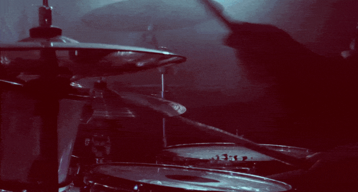 A compilation of different shots, including shoulders-up shot of an artist recording vocals in a studio, a close-up on a mouth singing into a recording studio microphone, a close-up on a drum set as someone sits and plays, scenes of dancing in dimly-lit clubs, and a fisheye portrait shot of an individual as they lean towards the camera.